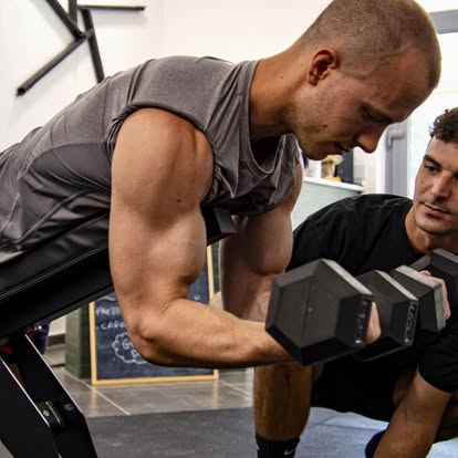 Personal trainer segue un cliente durante un esercizio con manubri
